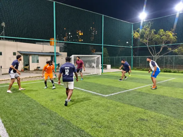 Football players contesting the ball near the goal on a floodlit five-a-side pitch.