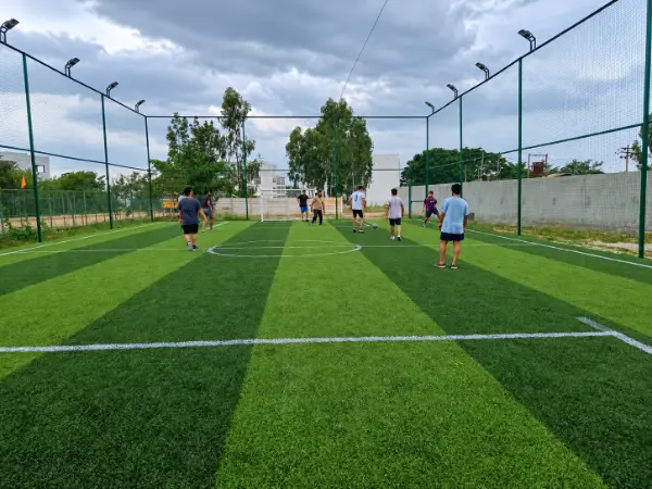 Friends playing football on a green outdoor turf pitch beneath an overcast sky.