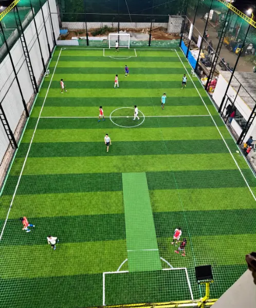 An elevated view of players spread across a green football pitch under evening floodlights.