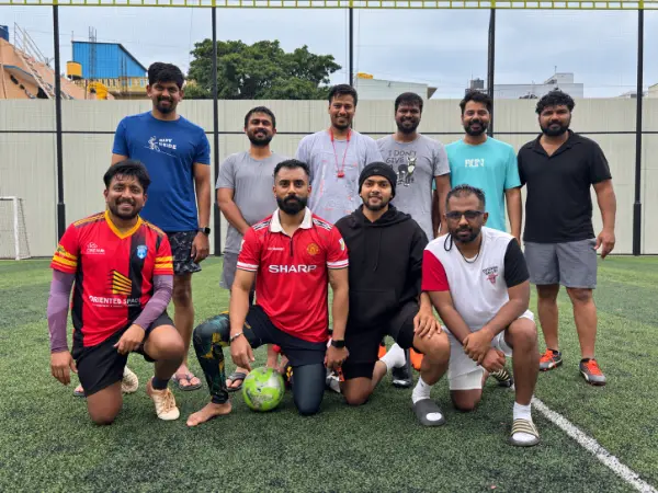 Ten club friends posing together with a football on the turf, some standing and some kneeling.